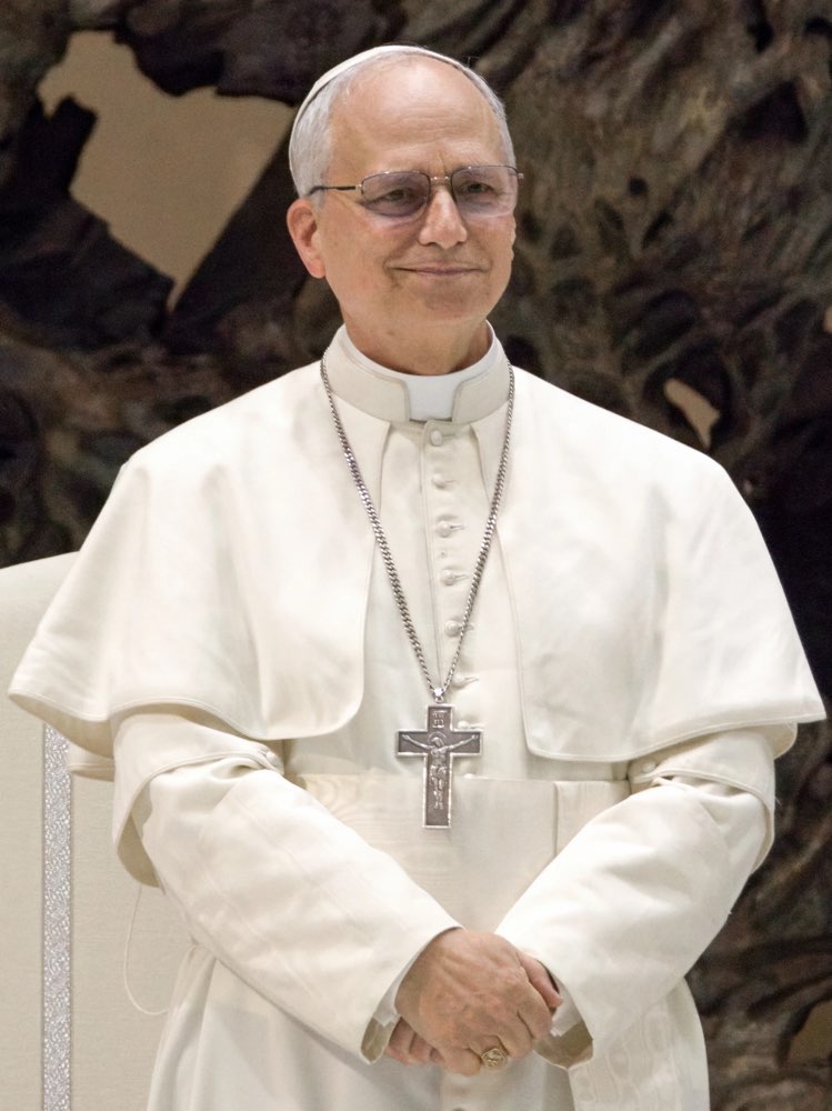Pope Leo XIV, standing in white papal dress with a pectoral cross.